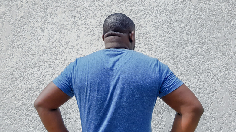 A person staring at a textured painted wall with their hands on their hips