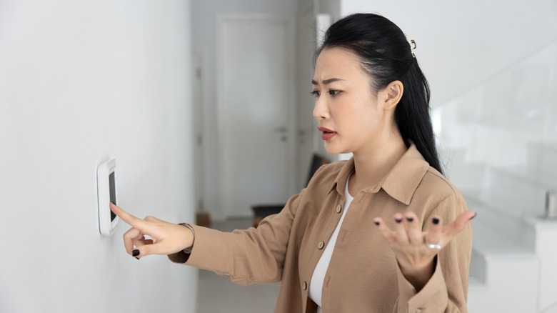 Young woman frustrated with adjusting thermostat