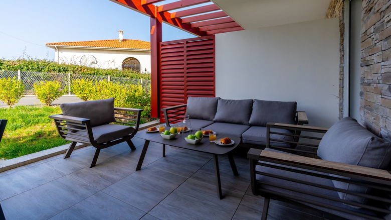 A shaded patio (or porch) with cushioned chairs and a couch