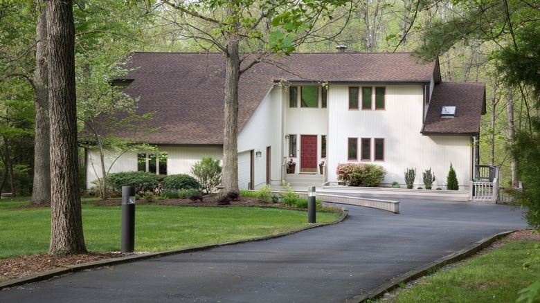 An asphalt driveway in front of stately house in the woods