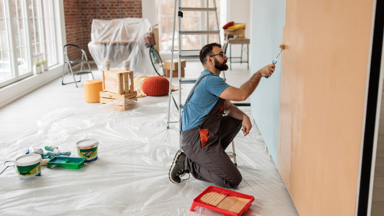 man kneeling and painting wall a shade of orange next to ladder