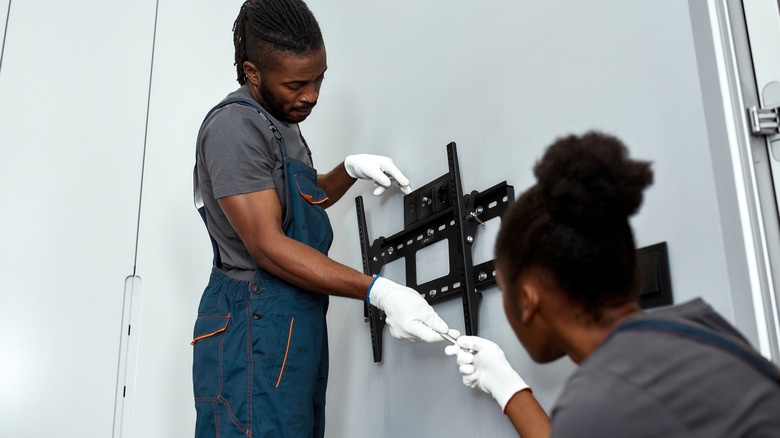 Two people installing TV mount on a wall