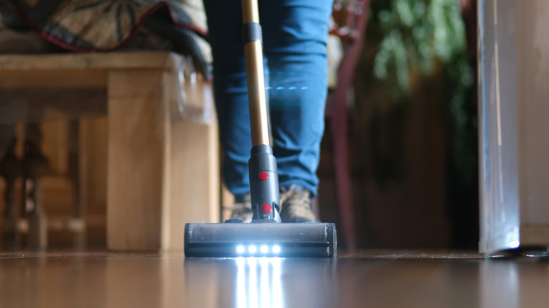Front view of person vacuuming with stick vacuum on wood floor