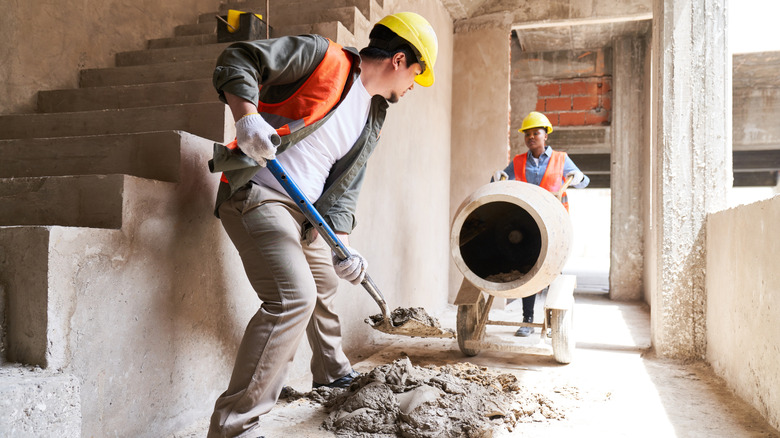 two construction workers use concrete next to a staircase