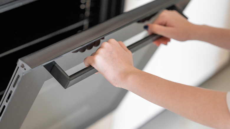 Hands opening a glass oven door