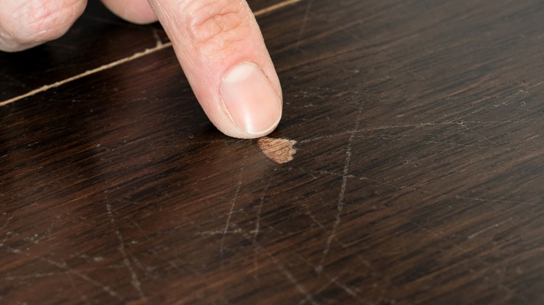 Finger pointing to gouges and scratches on a wood surface