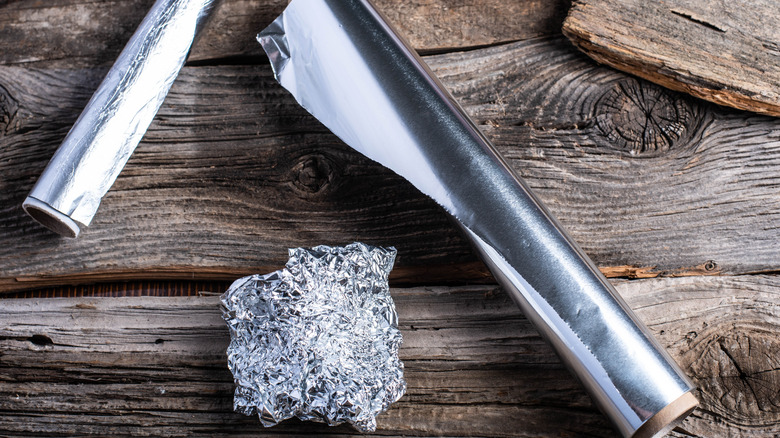 Two rolls of aluminum foil next to a crumbled ball of aluminum foil