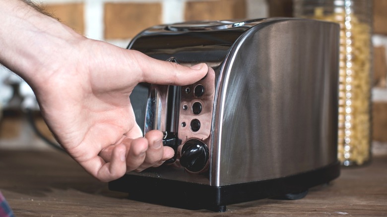 Person operating stainless steel countertop pop-up toaster