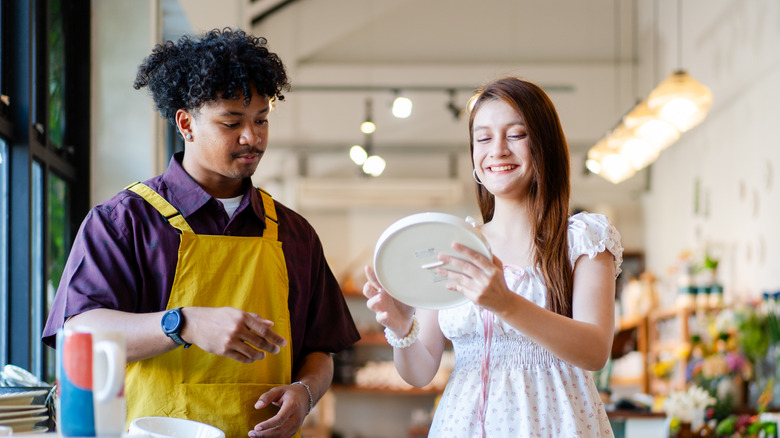 A woman smiles as she shows a dish to a man in a store