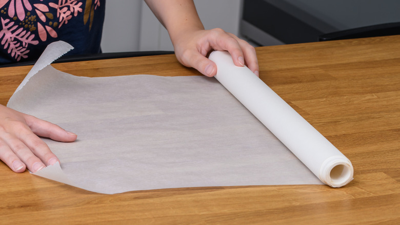Hands unrolling wax paper on a countertop