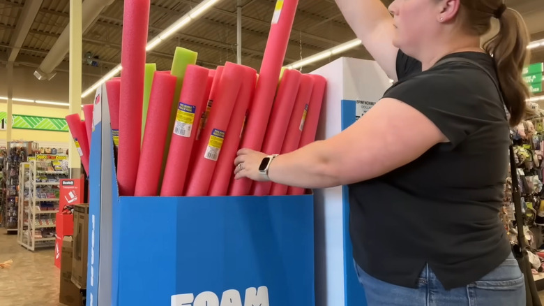 Young woman pulling red pool noodles from store display at the Dollar Tree