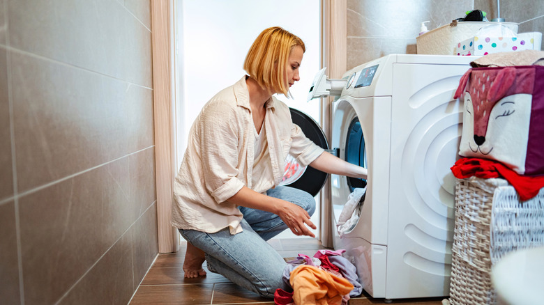 Woman putting clothes into a washing machine in a laundry room