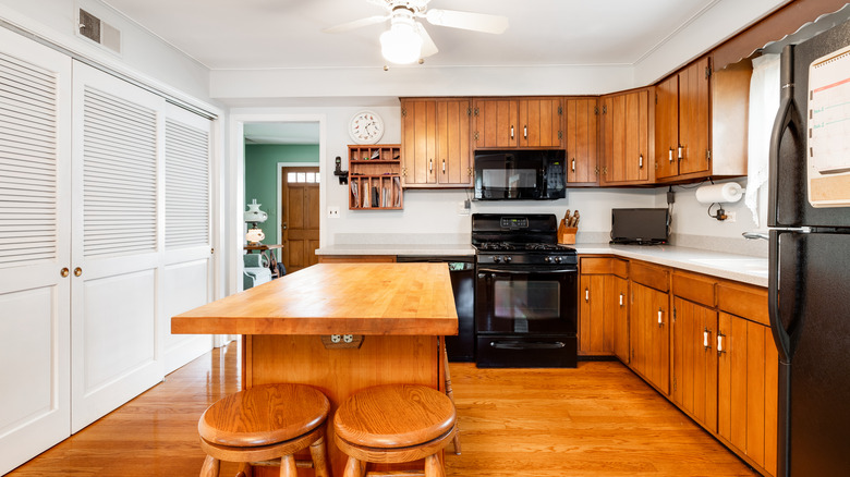 A honey oak kitchen with a white closet and walls, wood island, and large black appliances