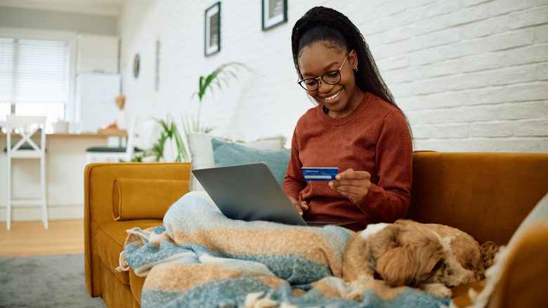 smiling person holding laptop and credit card