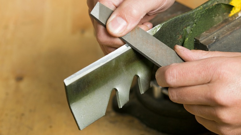 Person sharpening lawn mower blade with a file