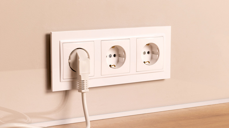A series of three European wall outlets with one electrical plug in the leftmost socket.
