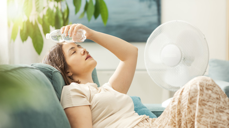 A young woman tries to cool off with a fan and cool bottle of water.