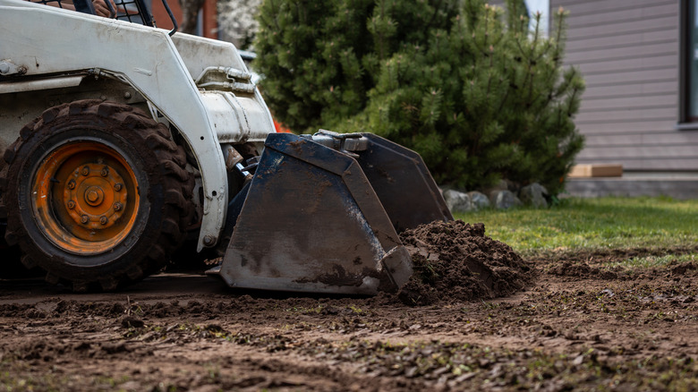 An excavator digs up grass to prepare for new residential landscaping.