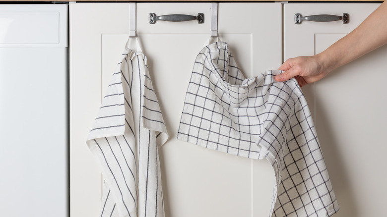 Hand reaching for a hanging kitchen towel on a cabinet door