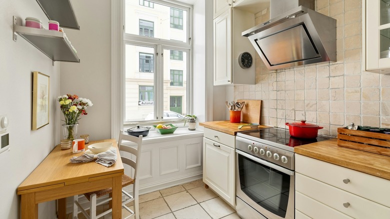 A small white kitchen with a little table up against the wall and a window