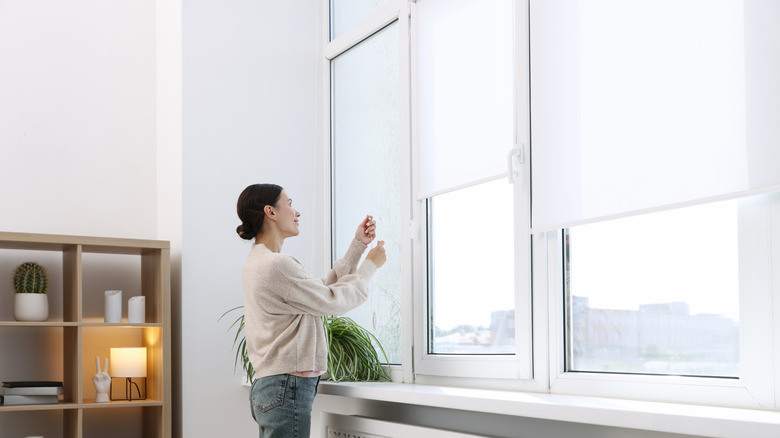A woman adjusts a blind on a window.