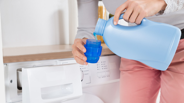 Hands pouring liquid laundry detergent into the lid for measurement