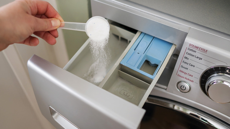 Hand adding a scoop of powdered laundry detergent into a washer's dispenser