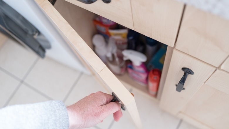 Person opening under-sink cabinet full of cleaning supplies