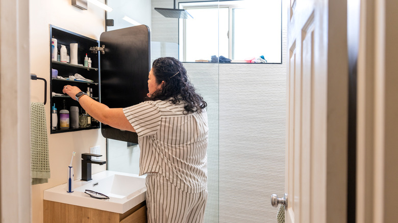 A person reaching into a medicine cabinet in a bathroom