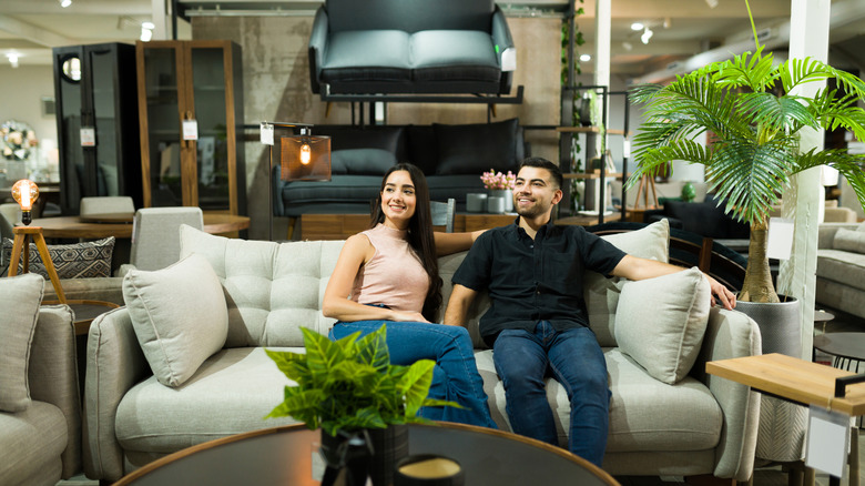 Two people sitting in a sofa in a furniture store full of modern living room pieces.