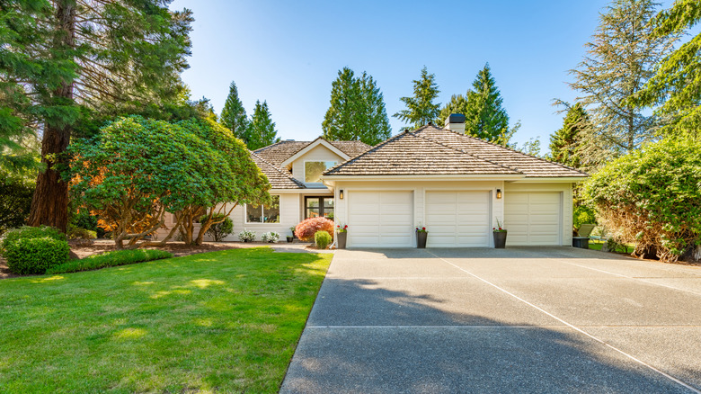 A concrete driveway leading up to an off-white home with a large side yard