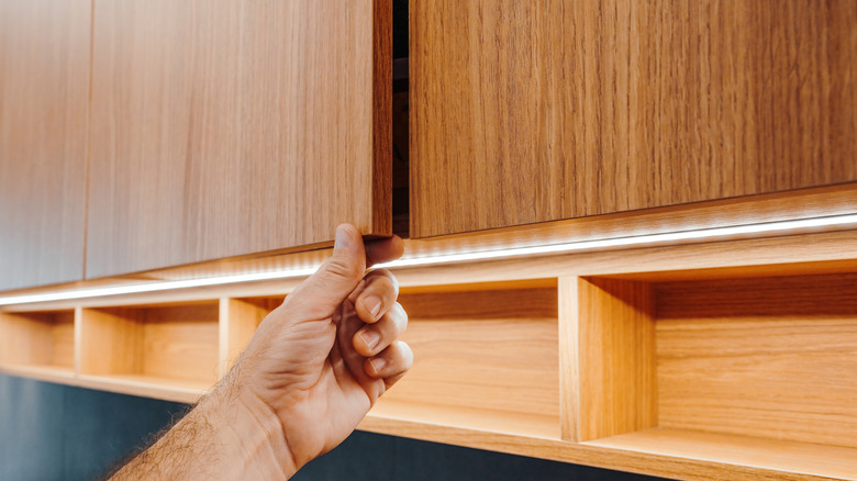 A man opening a two-tones oak cabinet.
