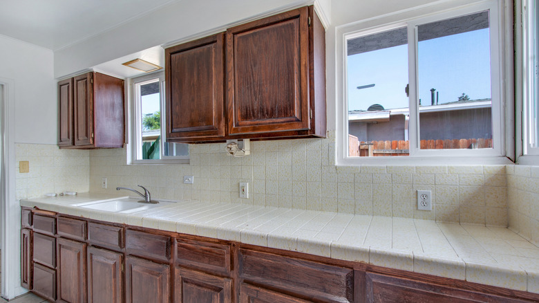 Outdated kitchen with white counter and walls, and dark, heavy-grained wood cabinets