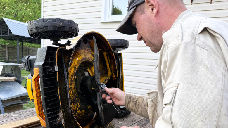 Man servicing blade of lawn mower on a bench outdoors