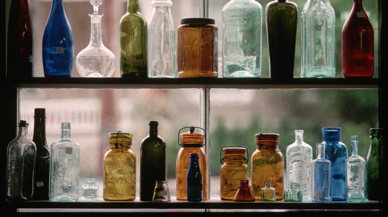 Antique glass jars in a variety of shapes and colors line a store display window.