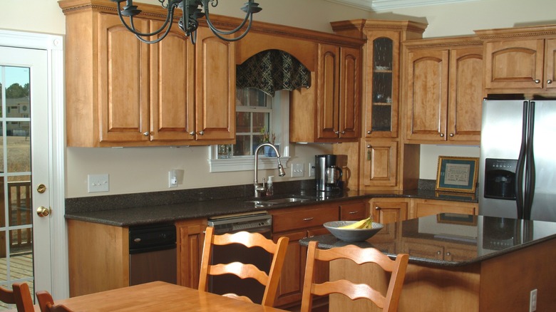 A dated honey oak kitchen with wooden cabinets, a table, and dark marble countertops