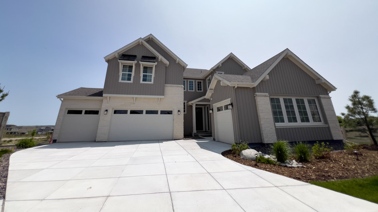 The exterior of a large gray house with a white cement driveway