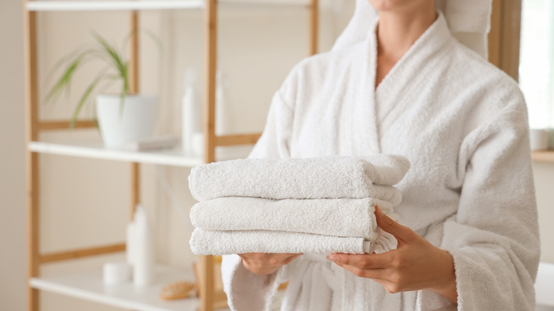 Woman in white robe holding stack of folded towels
