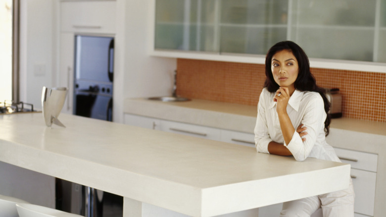 A woman contemplates while sitting by plain white builder-grade kitchen island