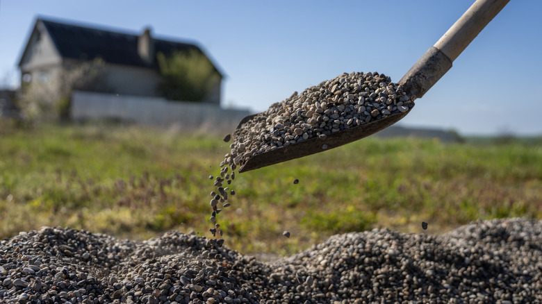 A person shoveling gravel with a house in the background