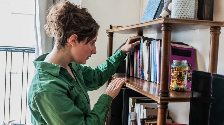 Woman looking through her books on a bookshelf