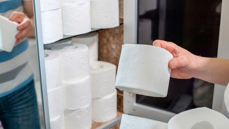 A person stacking toilet paper in a bathroom cabinet