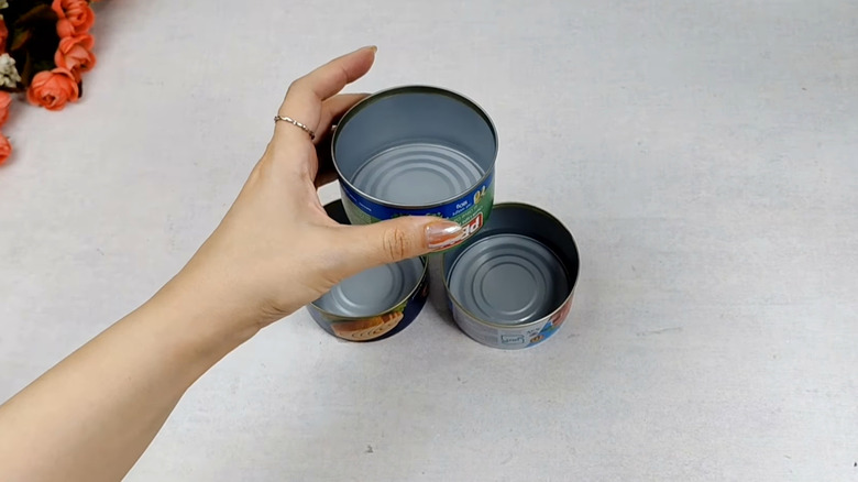 A hand with long painted nails picks up an empty tuna can on a table