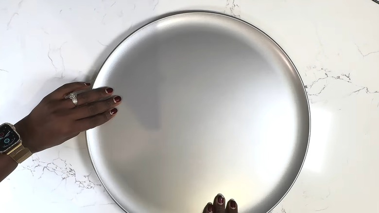 Person handling a Dollar Tree pizza pan on a countertop