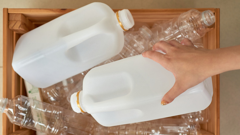 Person's hands sorting plastic milk jugs in wood bin with other plastic water bottles