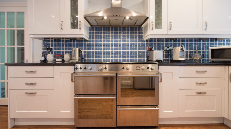 A kitchen oven with white cabinets and a blue tile backsplash