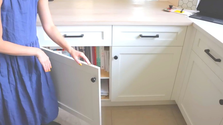 Woman opening white shaker cabinets with light countertop and modern classic kitchen design