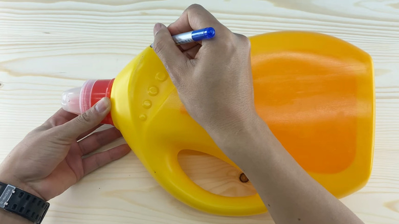 A person draws on a yellow laundry detergent bottle
