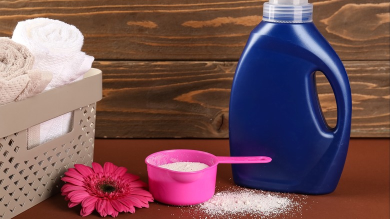 Liquid and powdered laundry detergent on a shelf with towels and a red flower