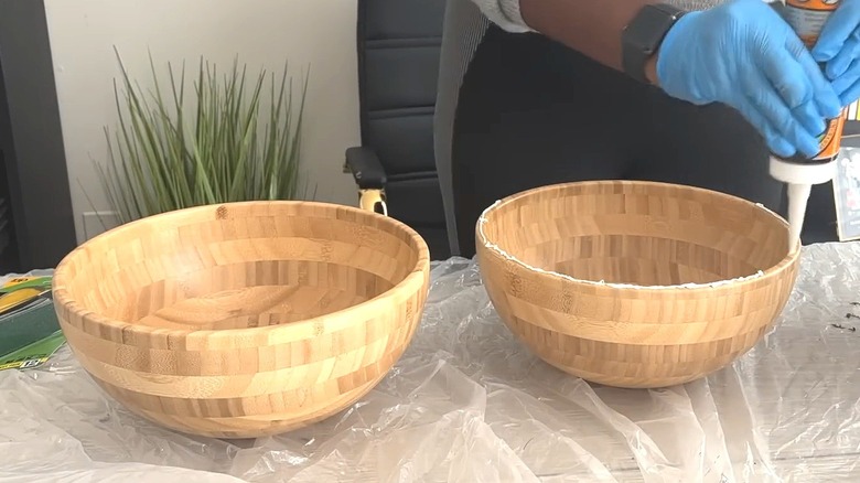 Woman with blue gloves super-gluing IKEA wood bowls together for DIY project on table with clear tarp